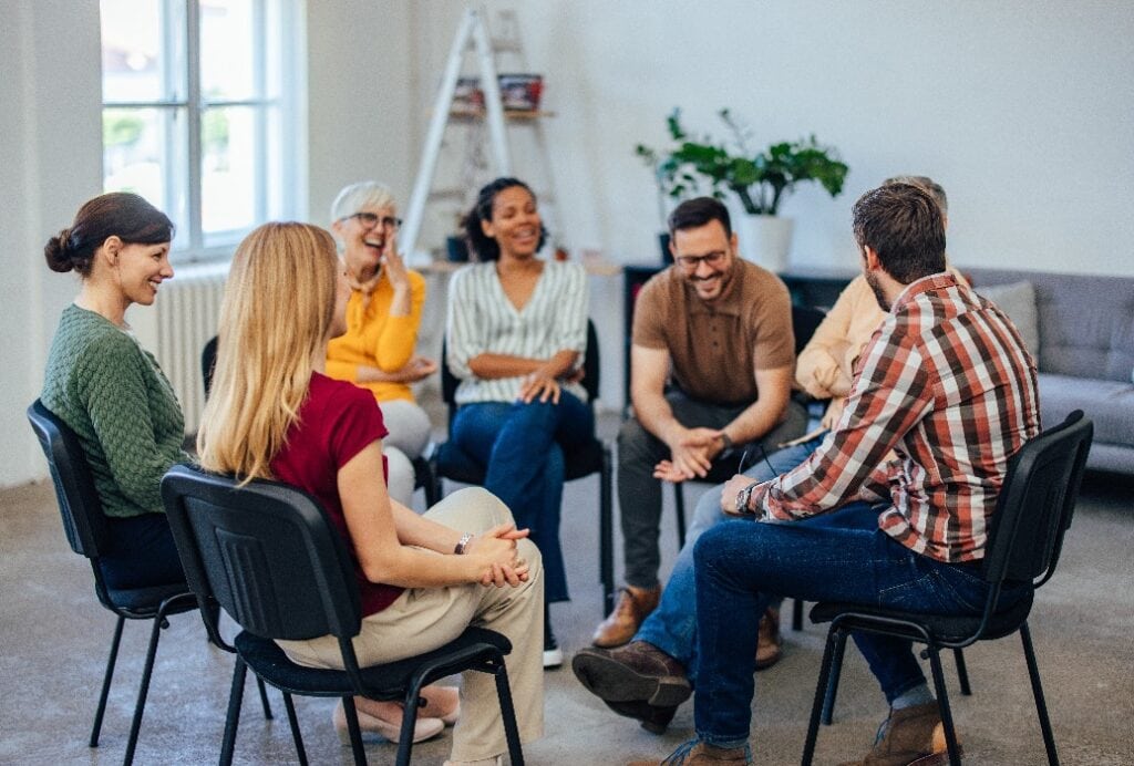 Group of people, sitting in a circle, laughing and talking to each other, during the group therapy.