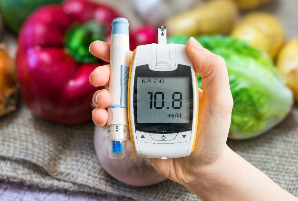 Diabetic diet and diabetes concept. Hand holds glucometer. Vegetables in background.